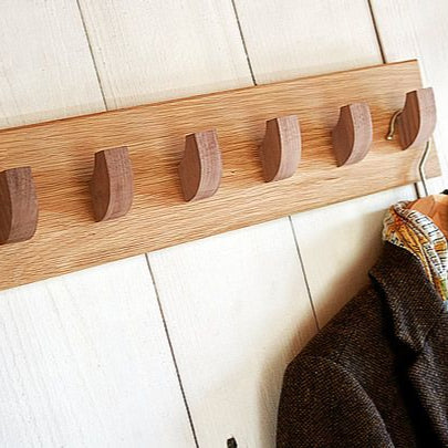 Wooden wall hook rack with five hooks on a white wooden floor.