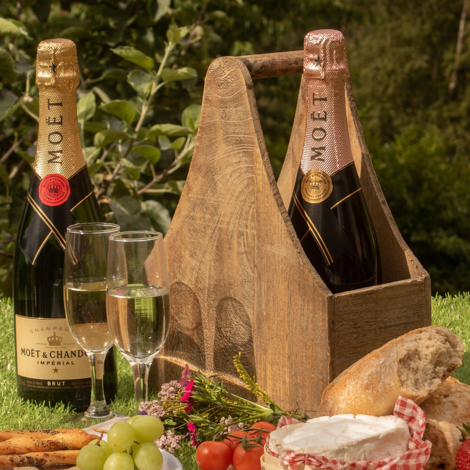 Picnic setup with Moet champagne, bread, cheese, fruits, and glasses on a grassy background.