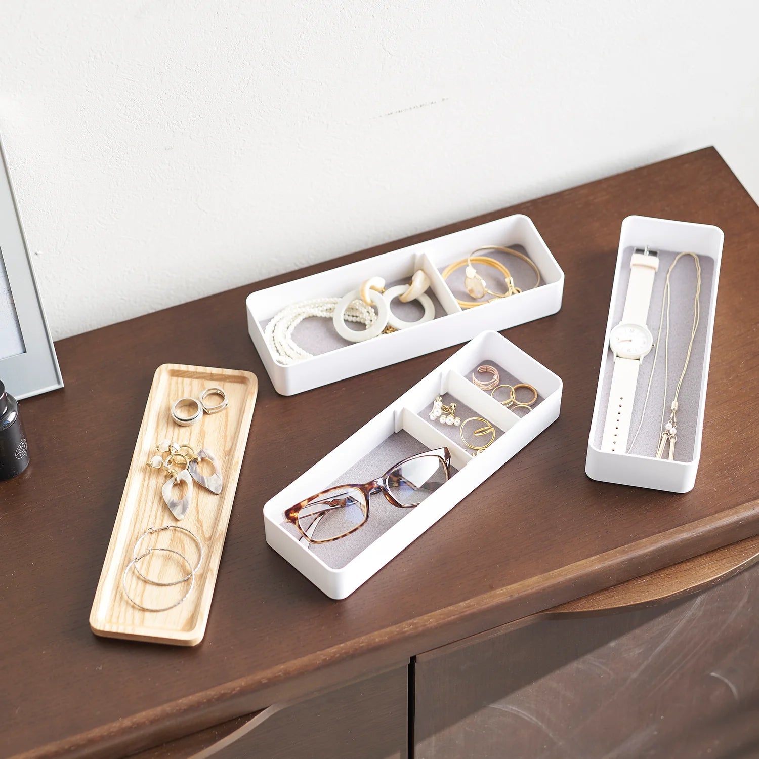 Jewelry and accessories organized in white and wooden trays on a wooden surface.