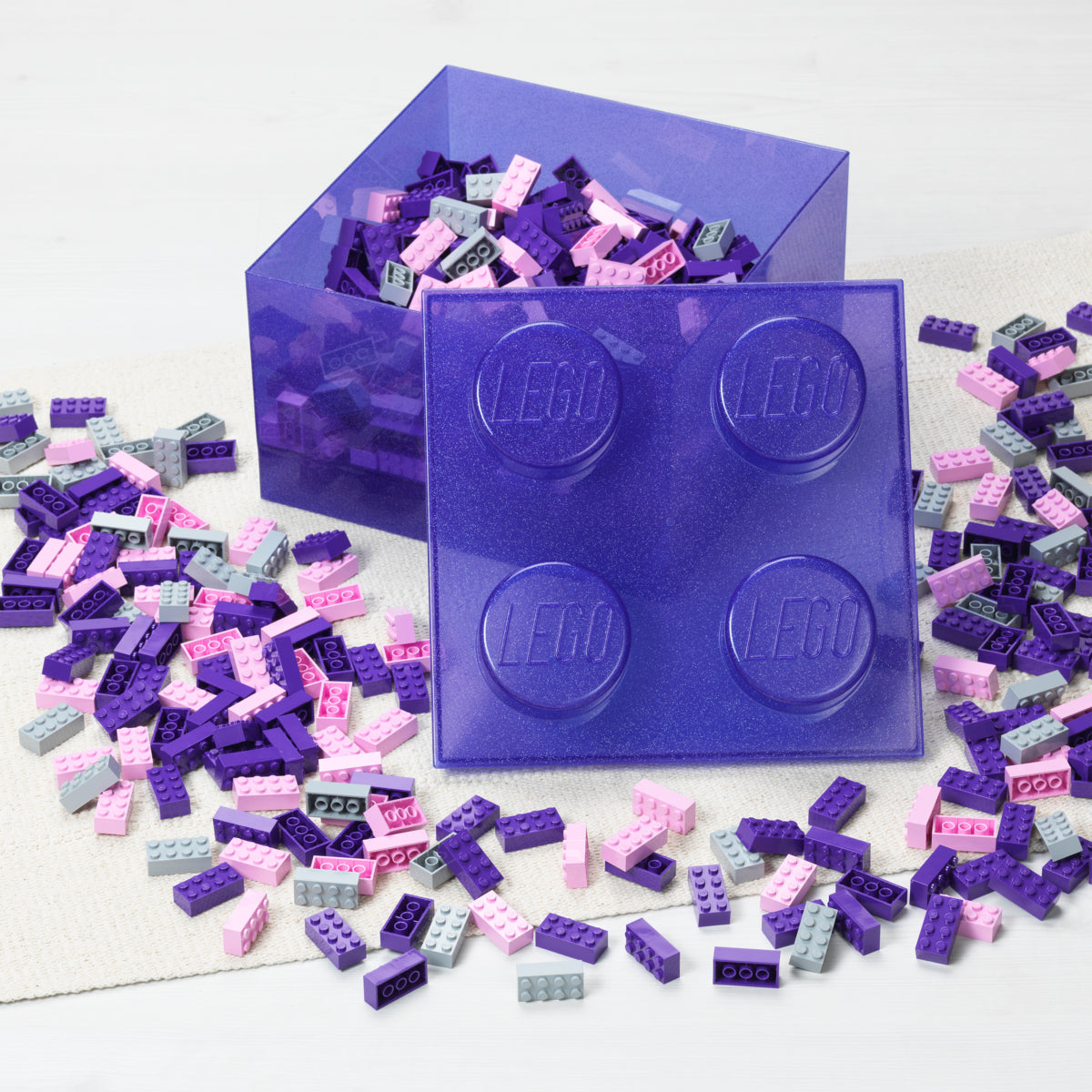 Purple LEGO brick container with scattered LEGO pieces on a white background