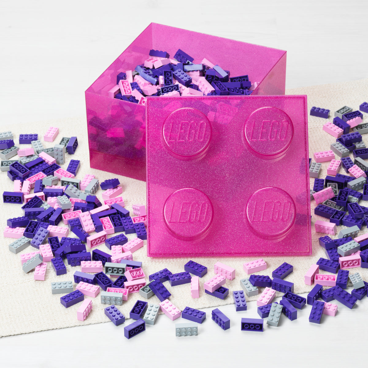 Pink LEGO brick container with scattered LEGO pieces on a white background