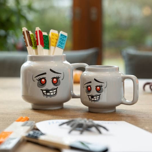 Two grey mugs with cartoon faces on a table with small tools and items.
