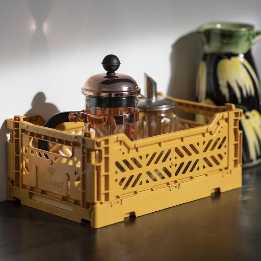 Yellow crate with glass jars on a wooden surface, with a ceramic pitcher in the background.