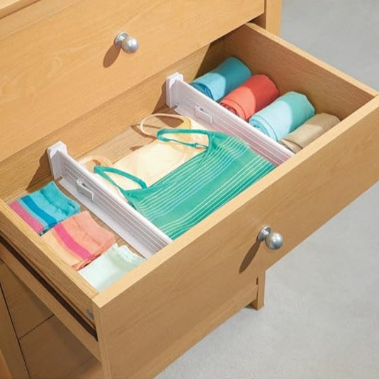 Open wooden drawer with colorful folded clothes on a light gray background