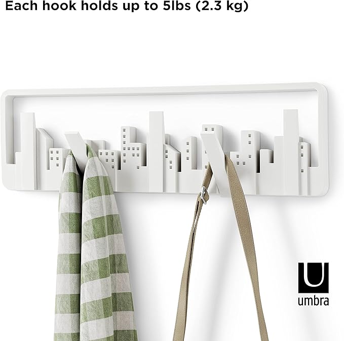 White wall hook with cityscape design holding a green and white striped towel and a beige bag, with text indicating weight capacity and Umbra logo.