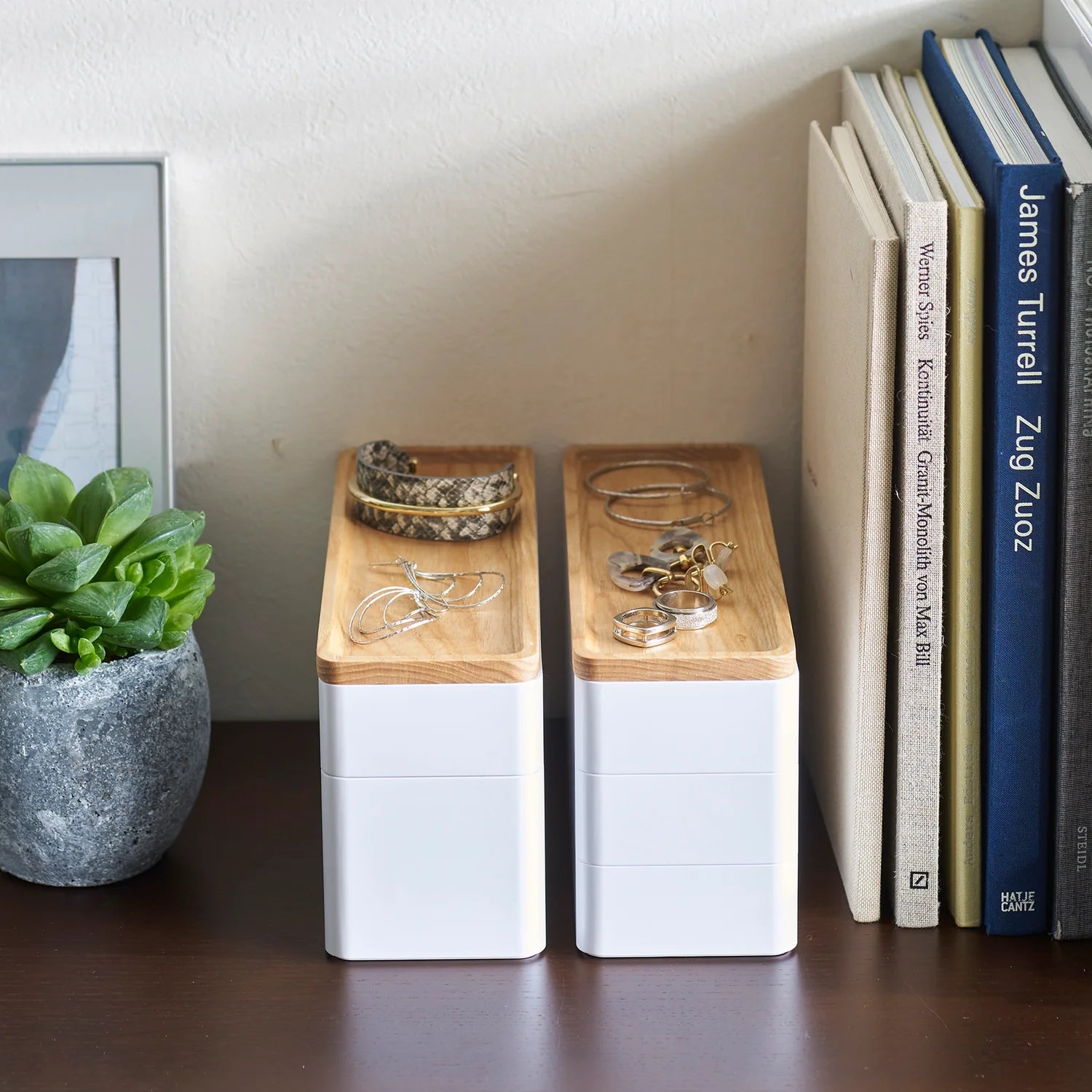 Two wooden and white bookends on a shelf with books and a plant.