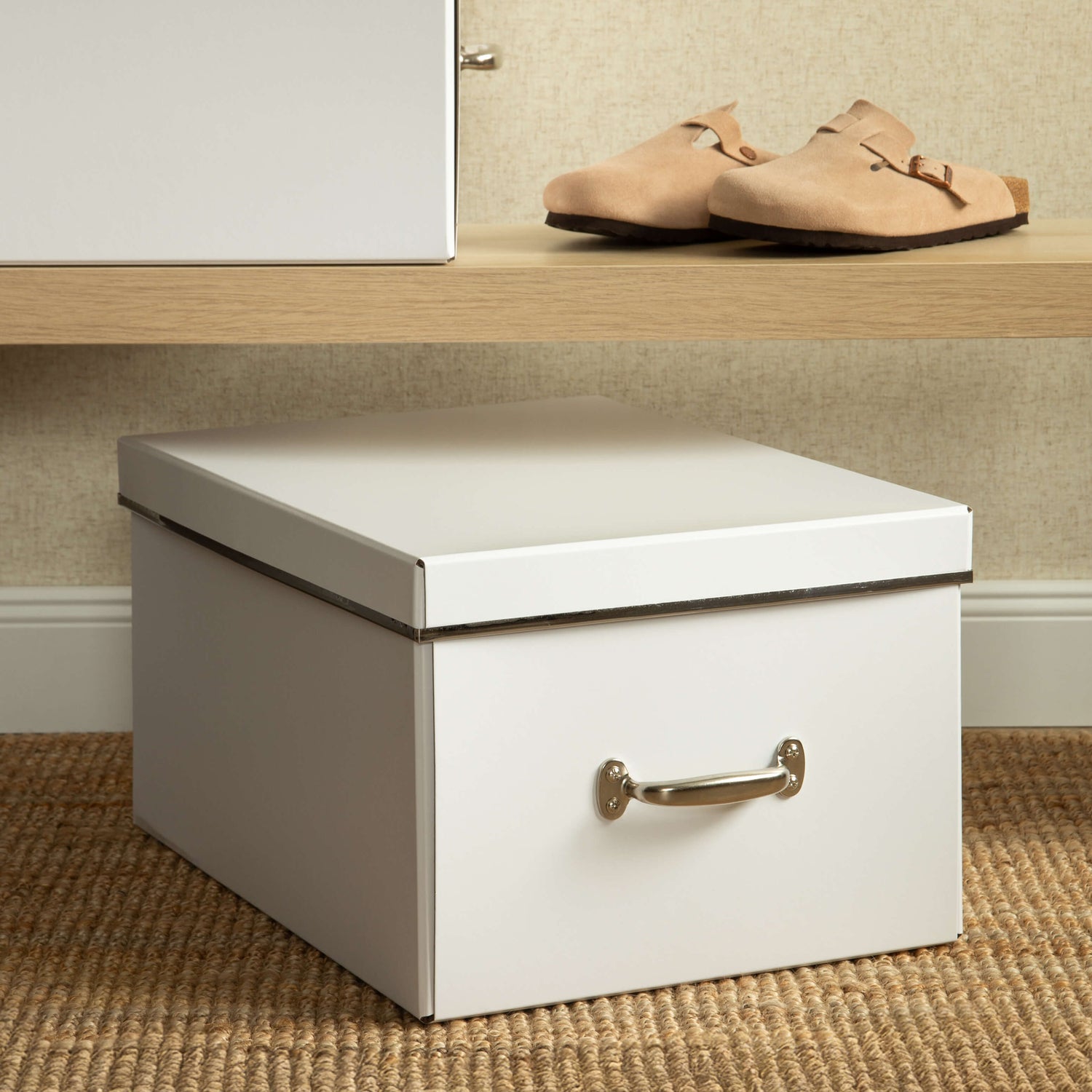 White storage box with a gold handle on a carpeted floor, with beige shoes in the background.