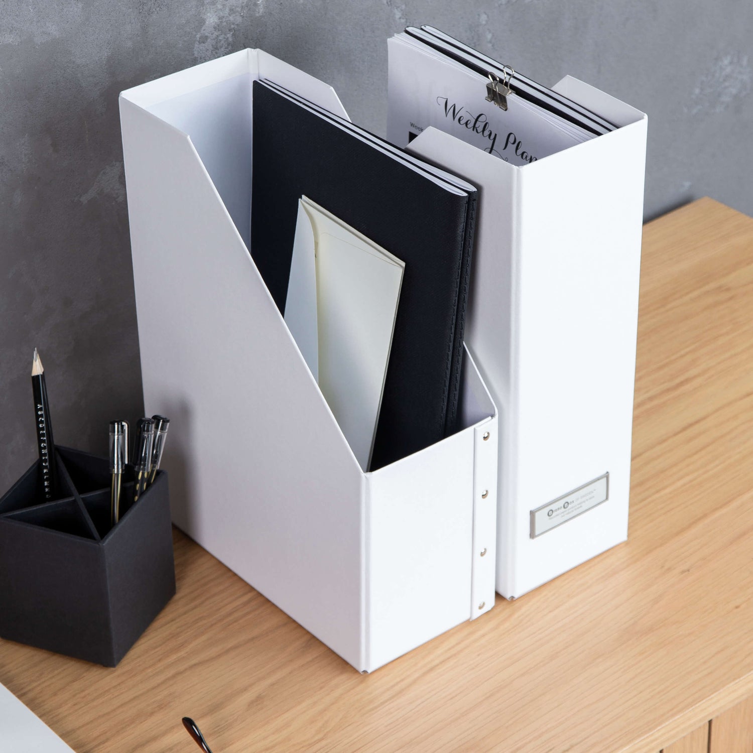 White magazine holder with books on a wooden surface against a gray wall.