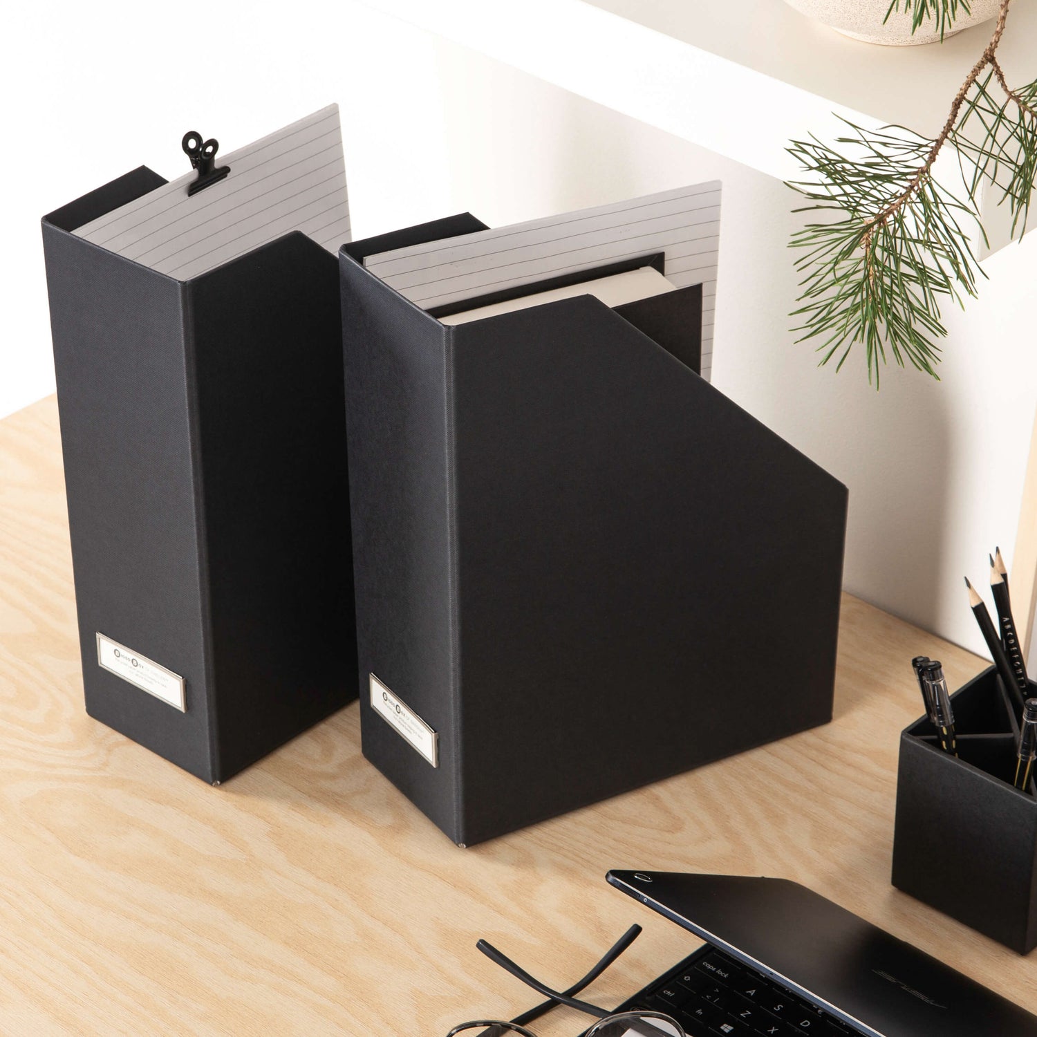 Black binders on a wooden desk with a laptop and pen holder.