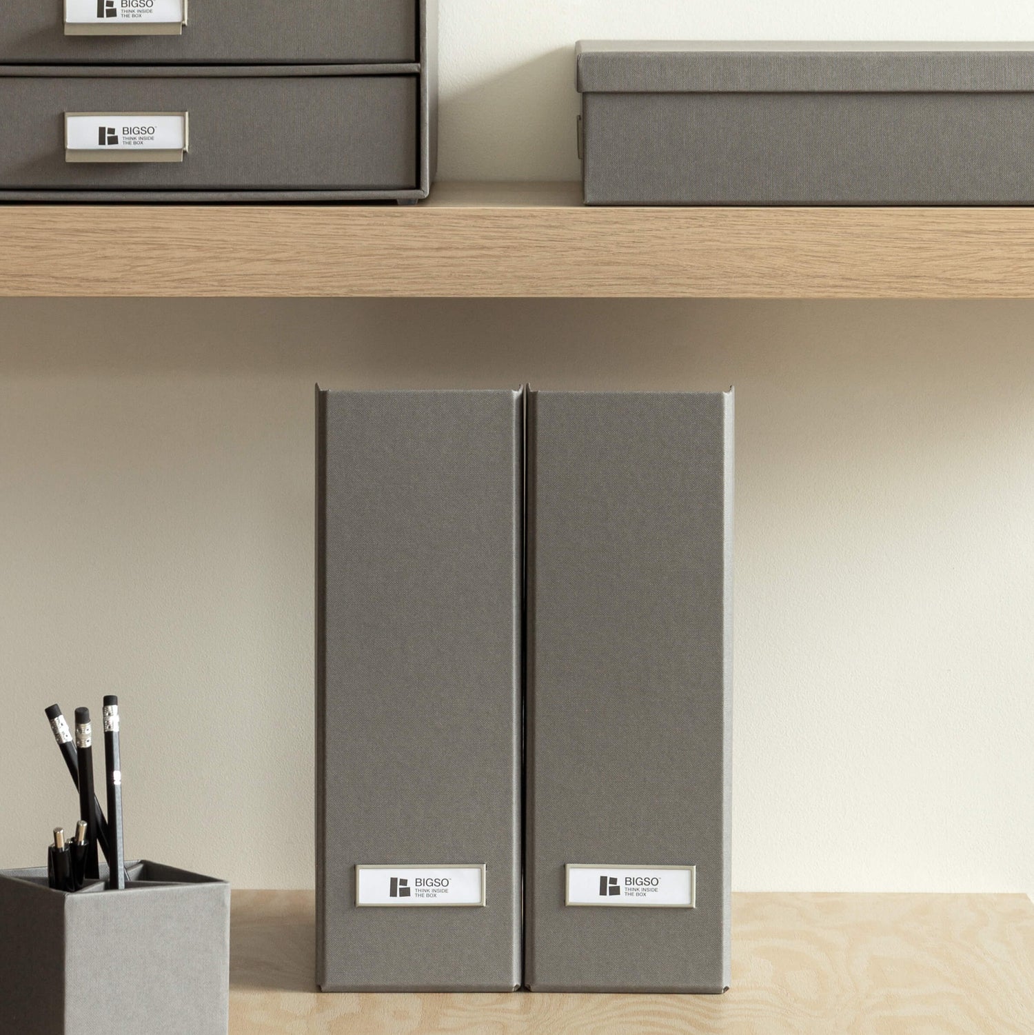 Gray office supplies including folders, a pen holder, and a notepad on a wooden shelf.