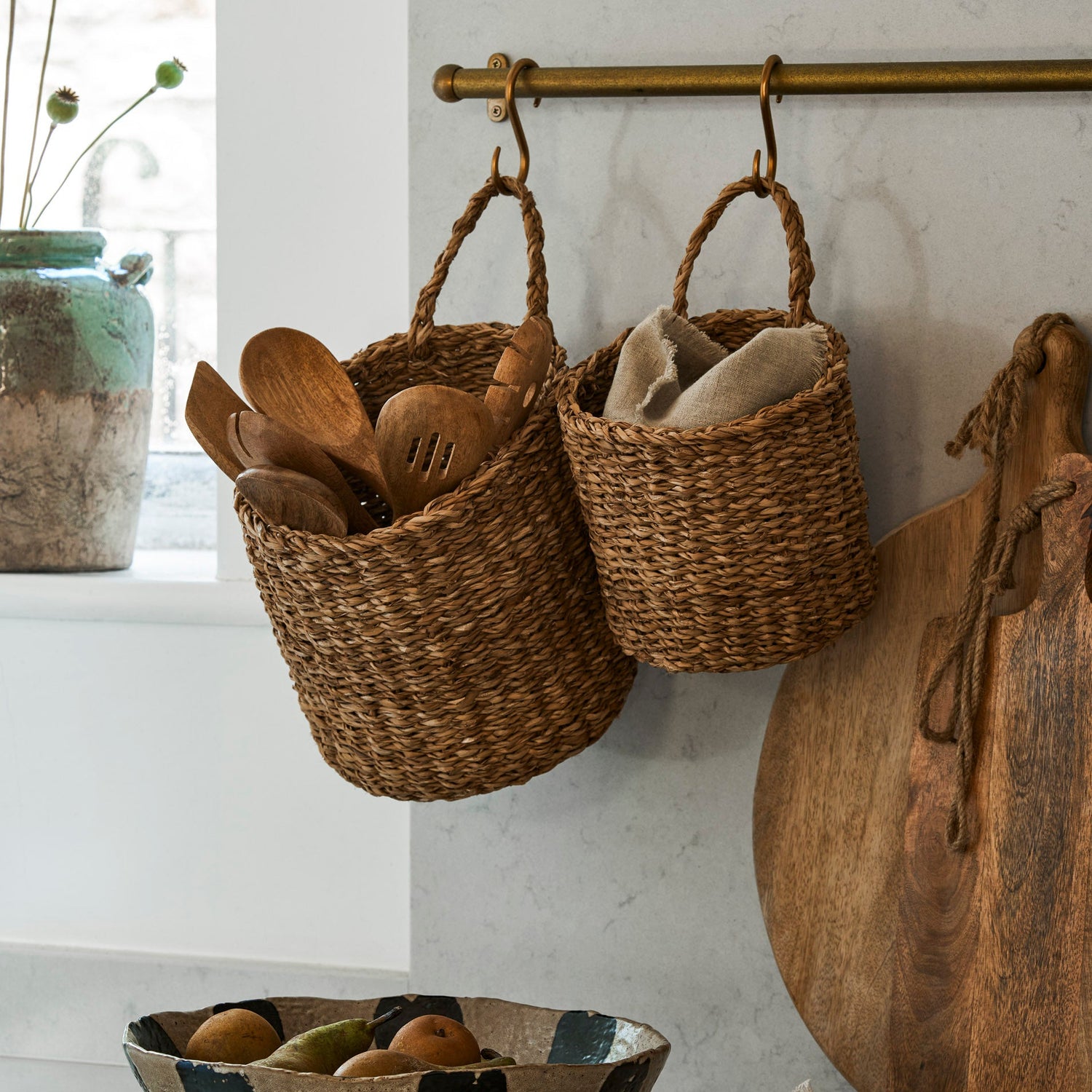 Hanging woven baskets with kitchen utensils on a marble countertop.