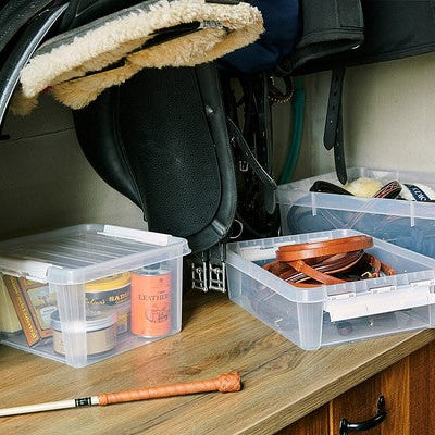Clear storage bins on a wooden surface with equestrian equipment.