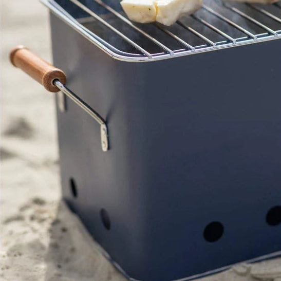 Portable grill with a wooden handle on a sandy surface