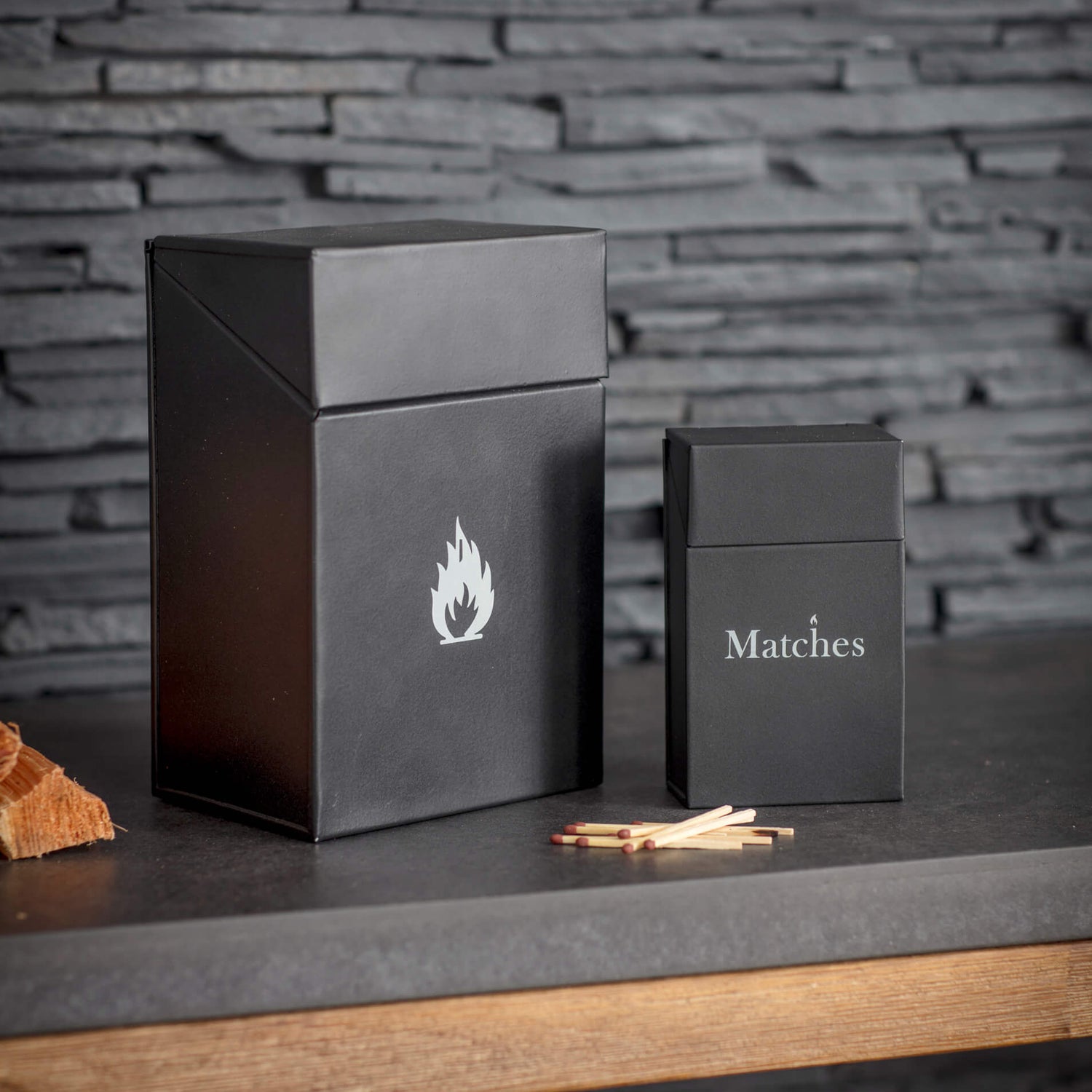 Black matchbox with a flame design on a stone surface against a brick wall.