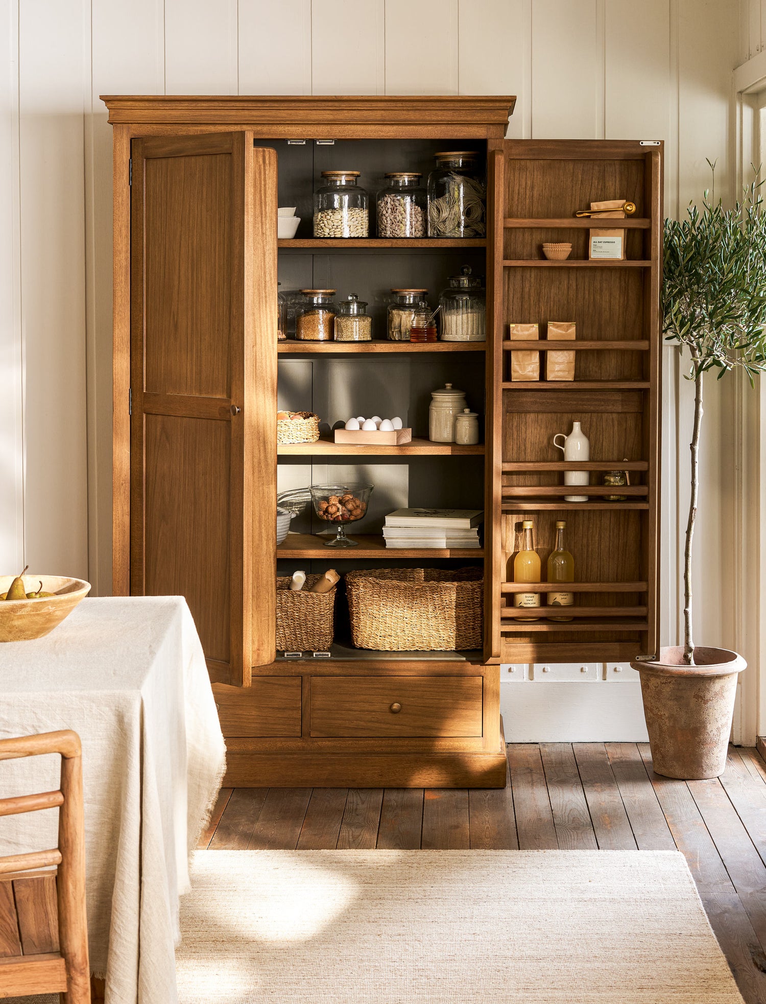 Wooden cabinet with shelves and drawers in a room with a plant and table.