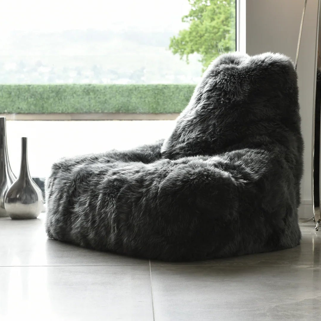 Gray fuzzy bean bag chair in a room with large windows and decorative vases.