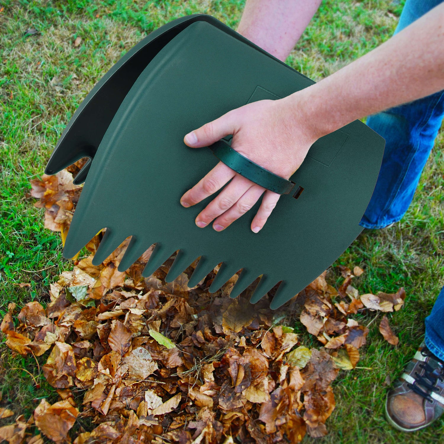 Person using a green leaf scoop to collect leaves on grass
