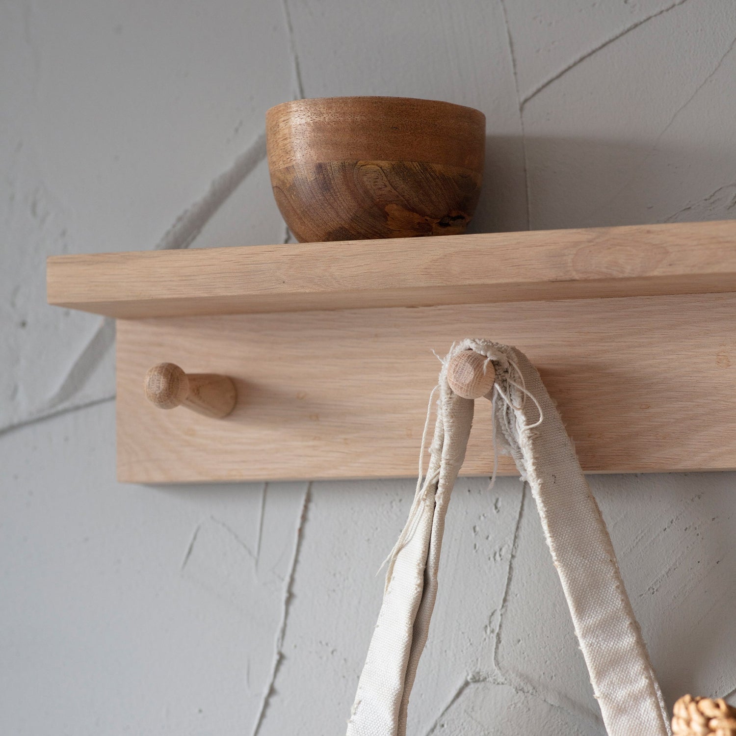 Wooden shelf with a wooden bowl and a white tote bag hanging on a hook against a light gray wall.