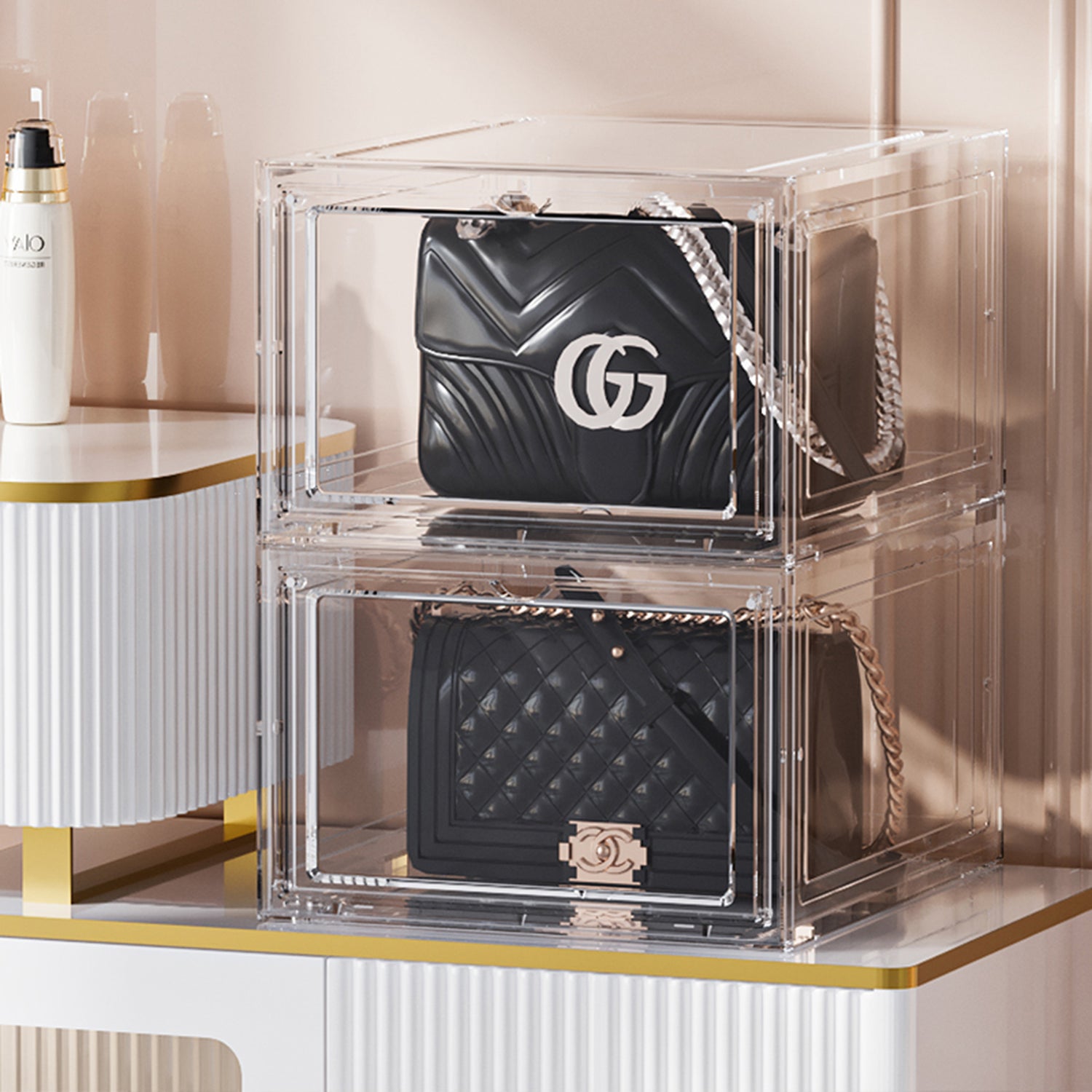 Two black handbags stacked in clear acrylic boxes on a light background