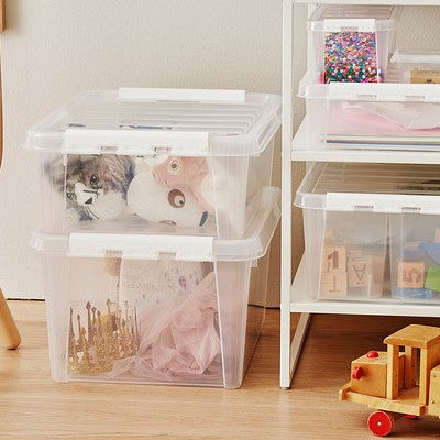 Clear storage bins with photos on a wooden floor next to a white shelf with toys.