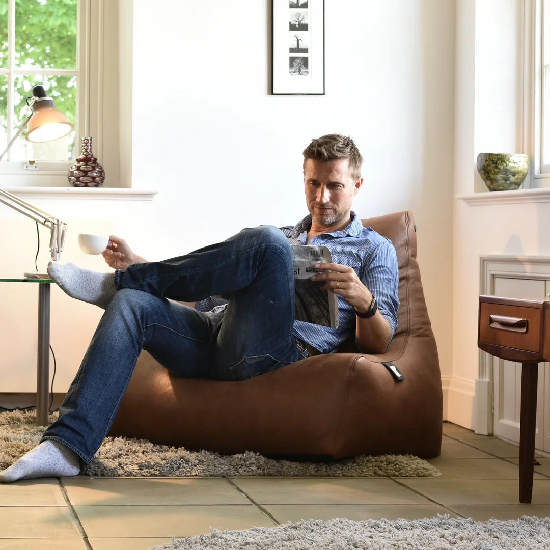 Man sitting on a brown bean bag chair in a cozy living room.