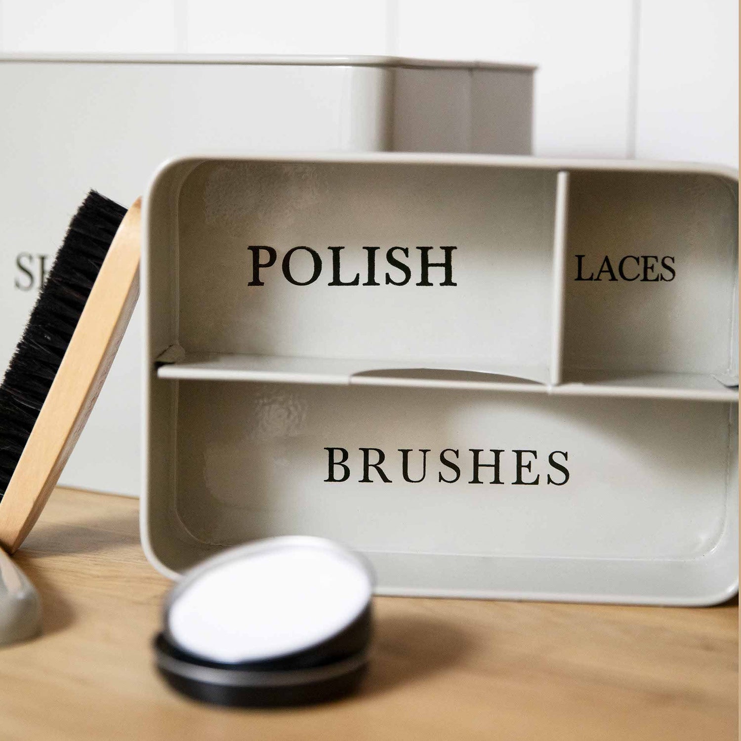 Metal storage tray with compartments labeled 'Polish', 'Laces', and 'Brushes' on a wooden surface.