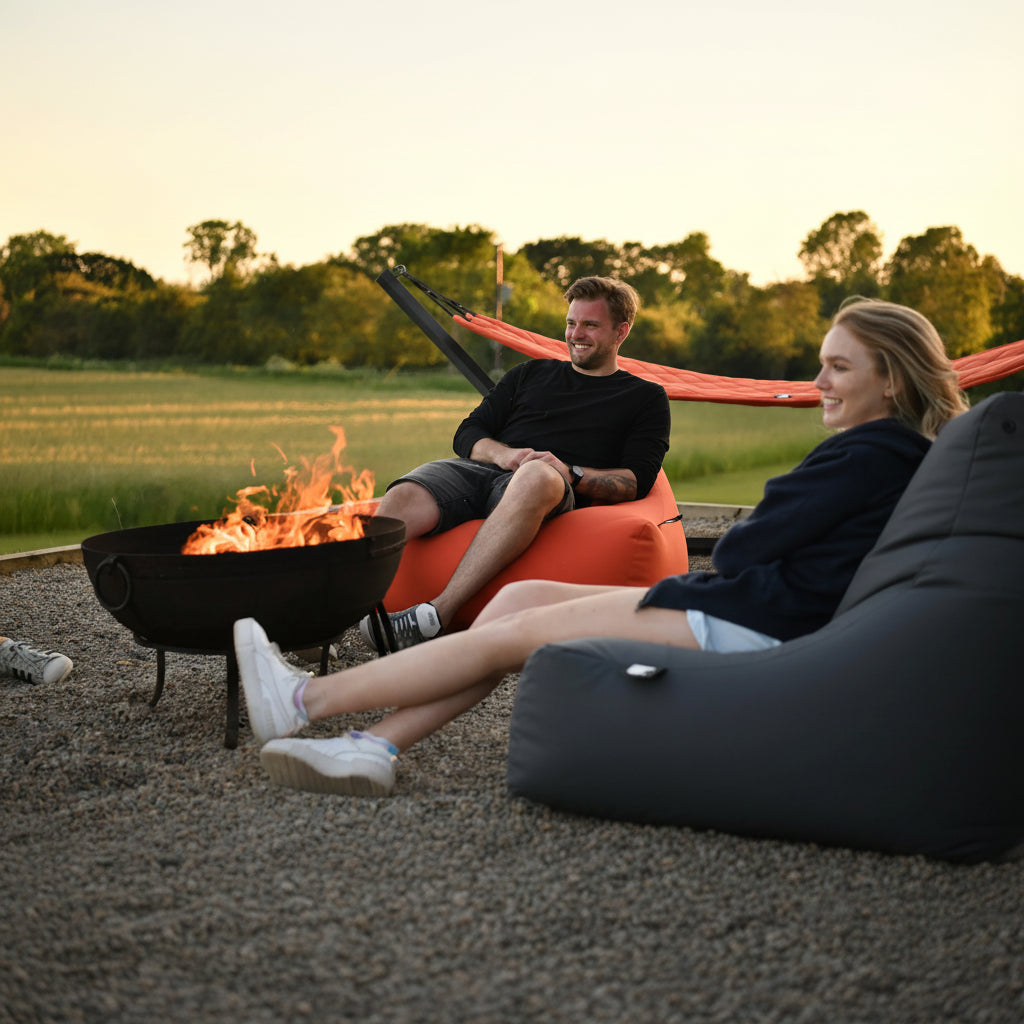 Two people sitting on bean bags by a fire pit in a natural setting