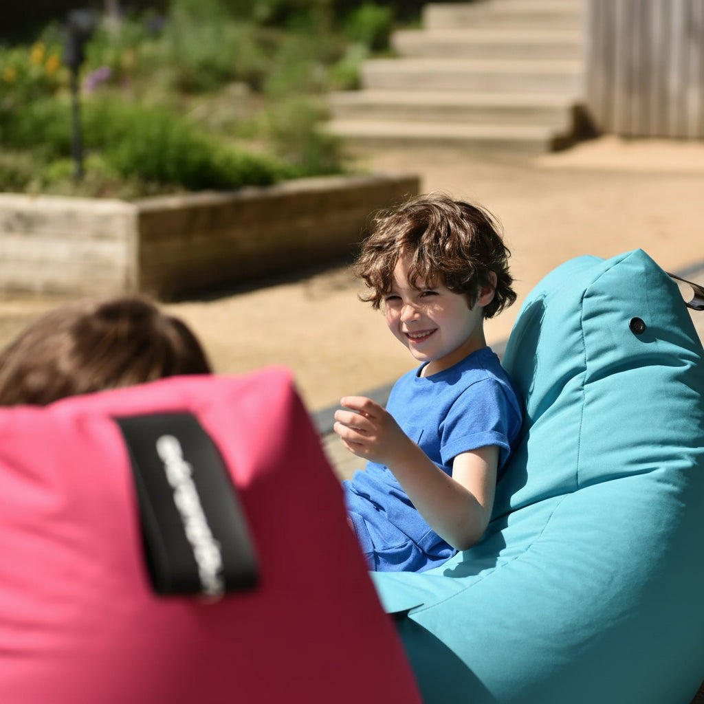 Child sitting on a blue bean bag chair outdoors with another child partially visible.