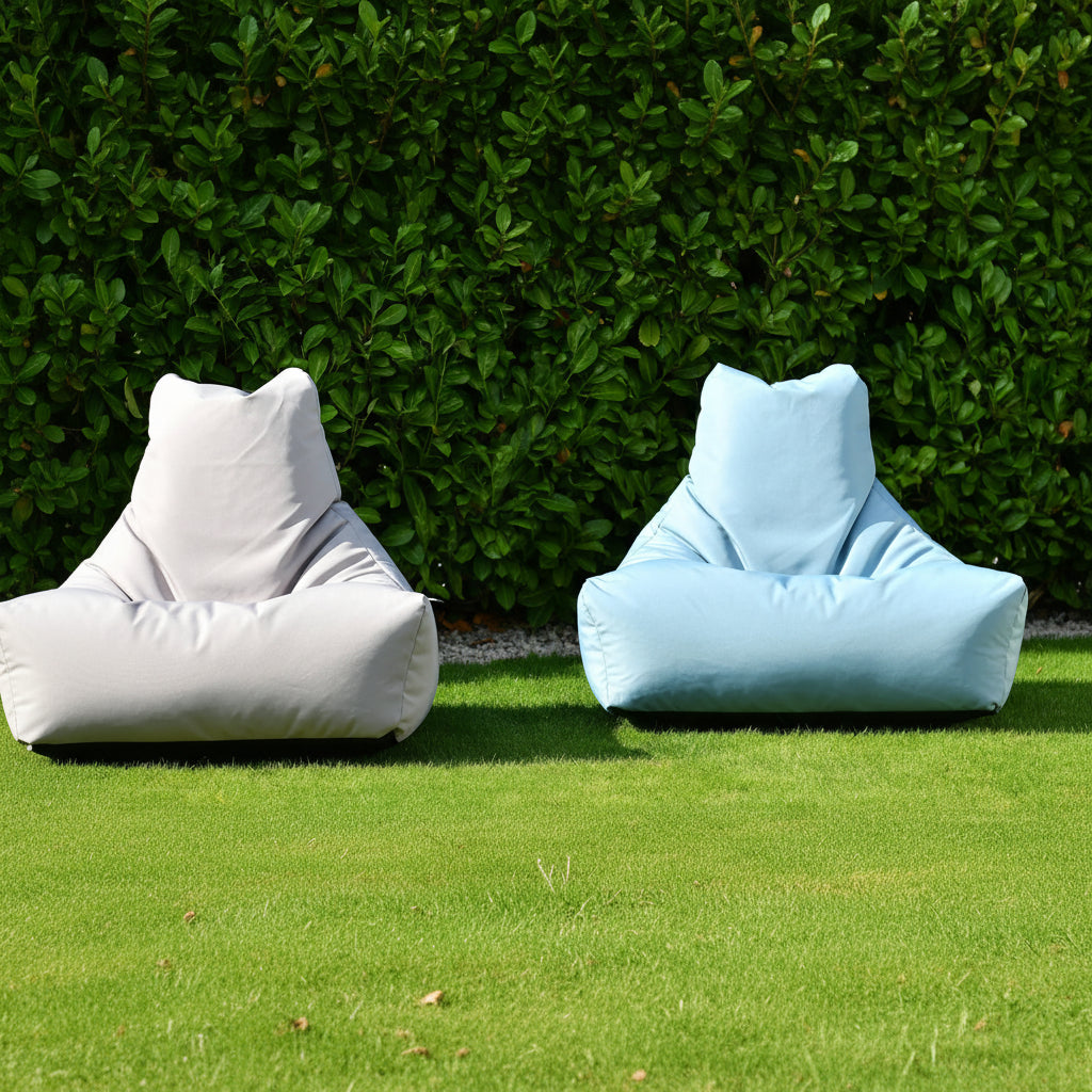Two bean bags, one gray and one light blue, on grass with a green bush background.