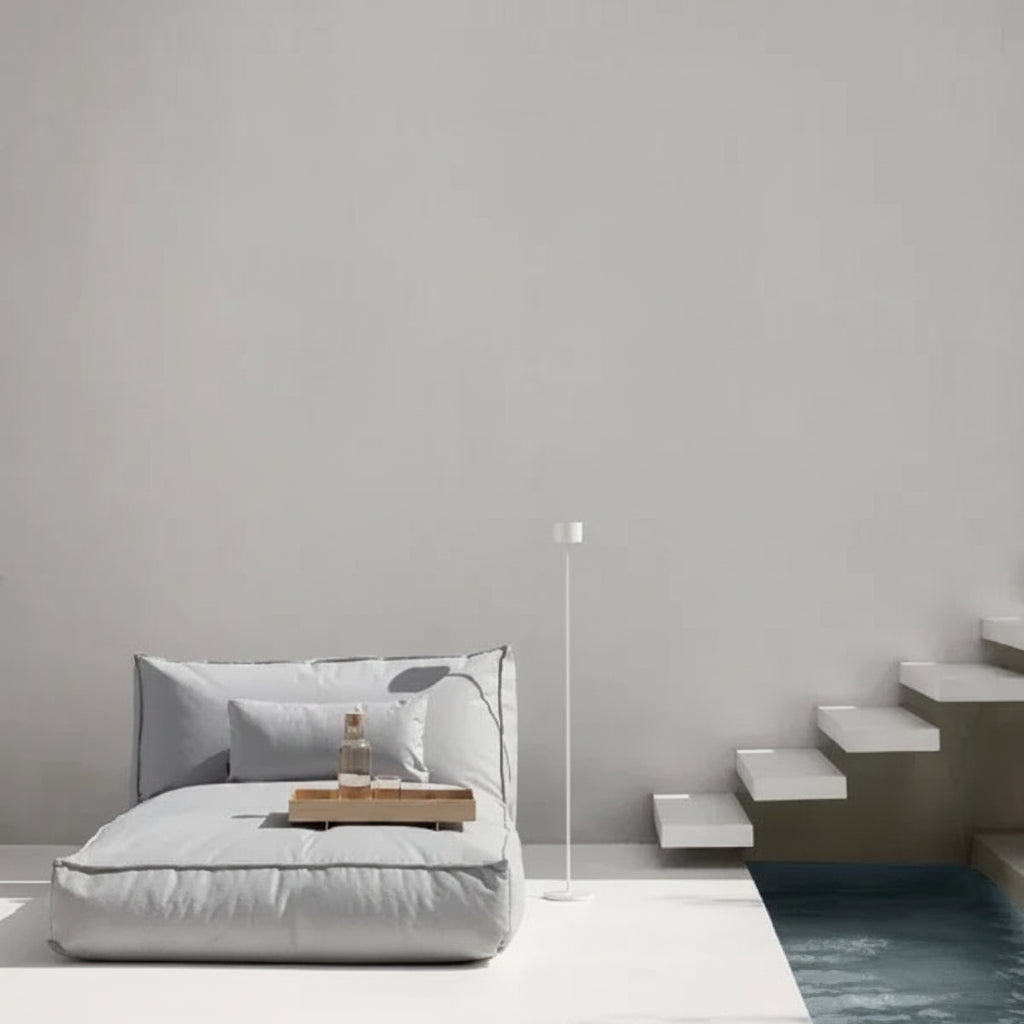 Modern indoor setting with a bed, side table, and floor lamp against a gray wall.