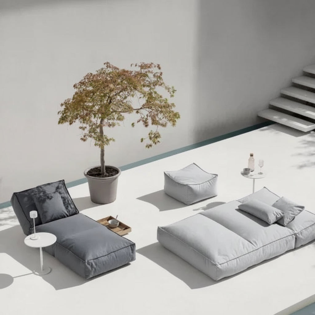 Modern outdoor furniture set with gray cushions on a white floor, featuring a small tree and side tables.