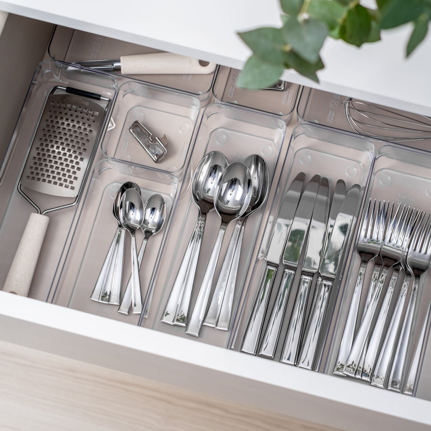 Silverware set in a drawer organizer with a decorative plant in the background