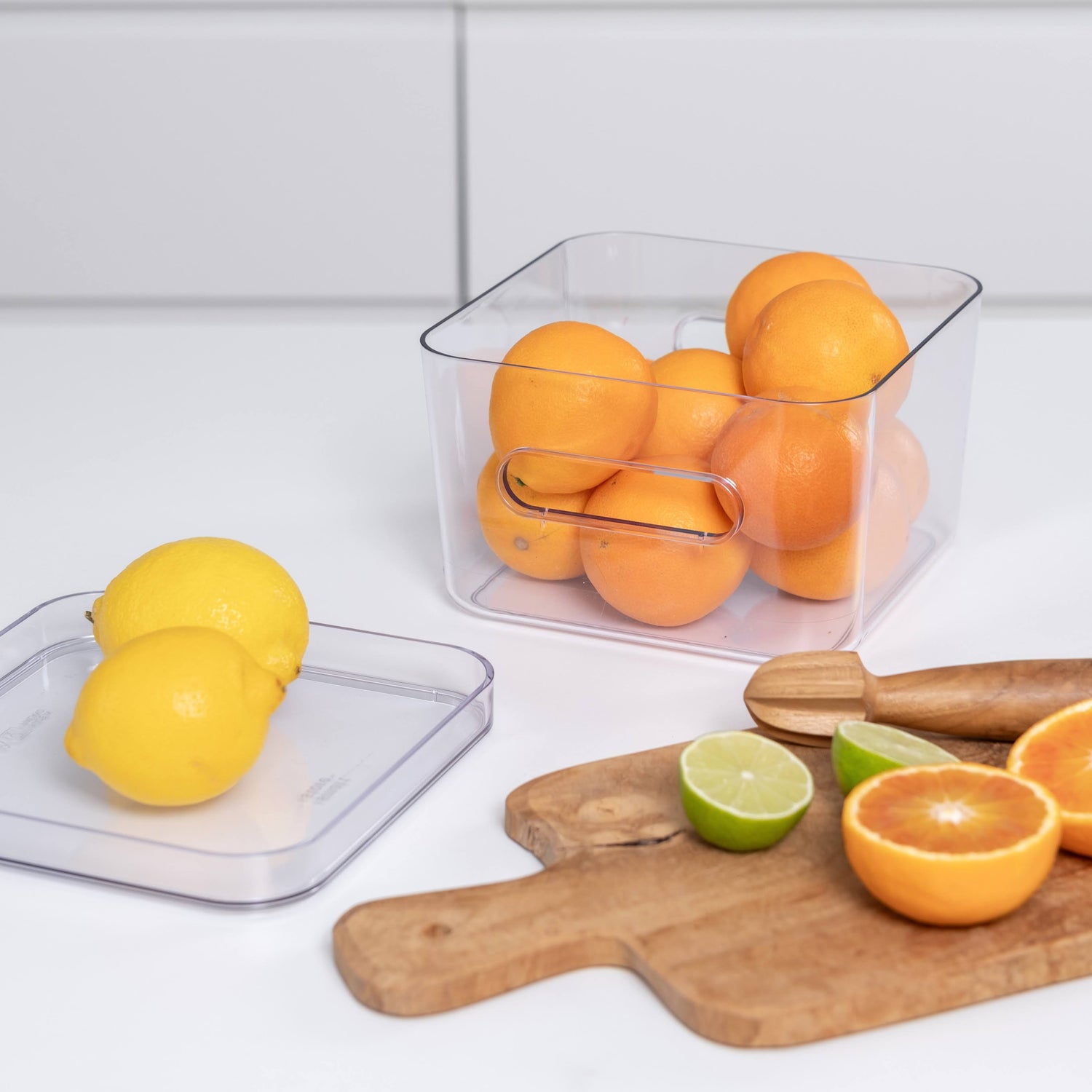 Clear container with oranges on a kitchen counter with lemons and limes.