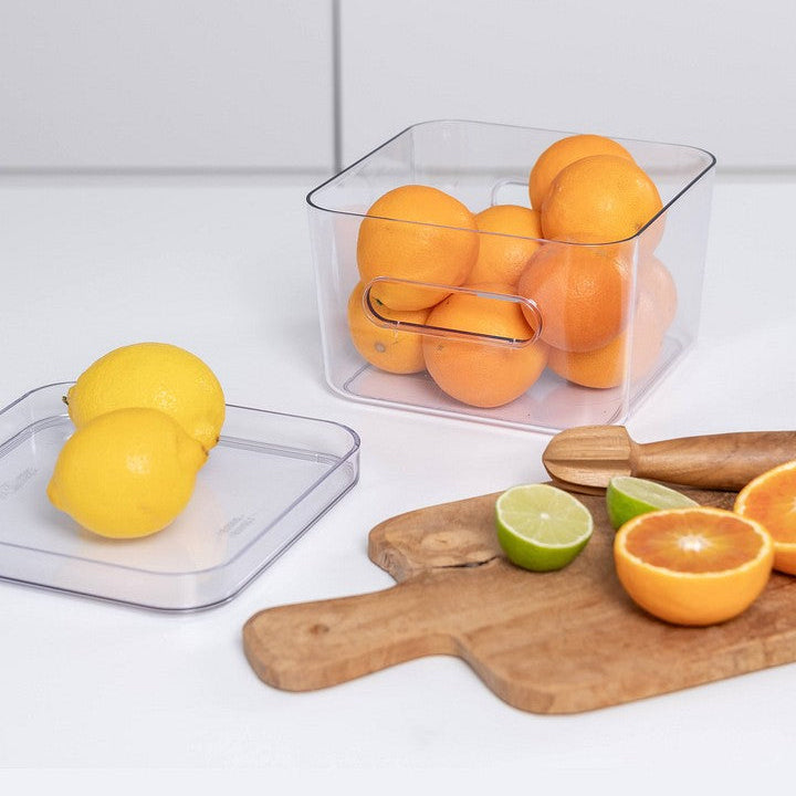 Clear container with oranges on a kitchen counter with lemons and limes.