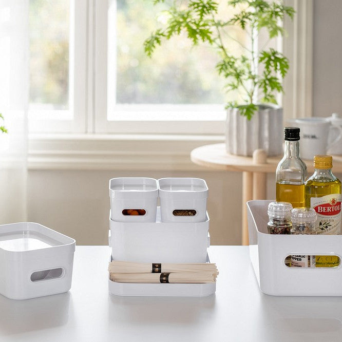 White storage bins on a table with bottles and books in a bright room.