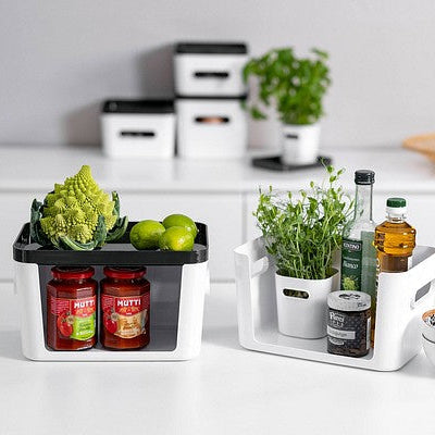 Kitchen counter with herb pots, jars, and a cutting board on a white surface.