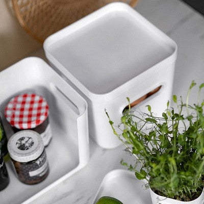 White kitchen utensils and containers on a marble countertop with limes and a plant.