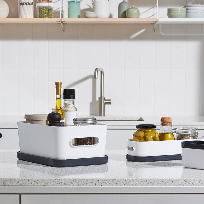 White kitchen sink with black and gray containers on a white countertop.