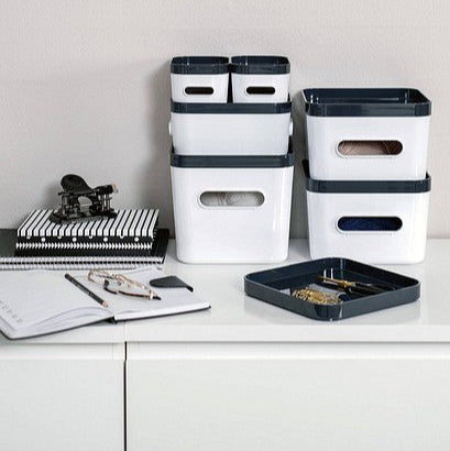 White storage bins with black lids on a white surface against a light gray wall.