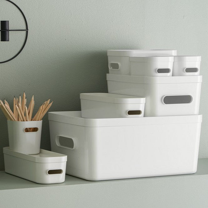White storage boxes on a gray surface with a plant and small container in the background.