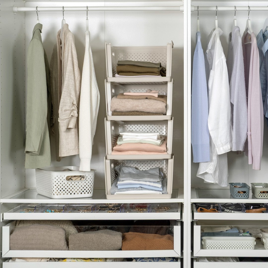 A white modular closet organizer with multiple sections, shelves, and hanging rods, styled with neutral-colored clothing, folded textiles, and storage baskets.