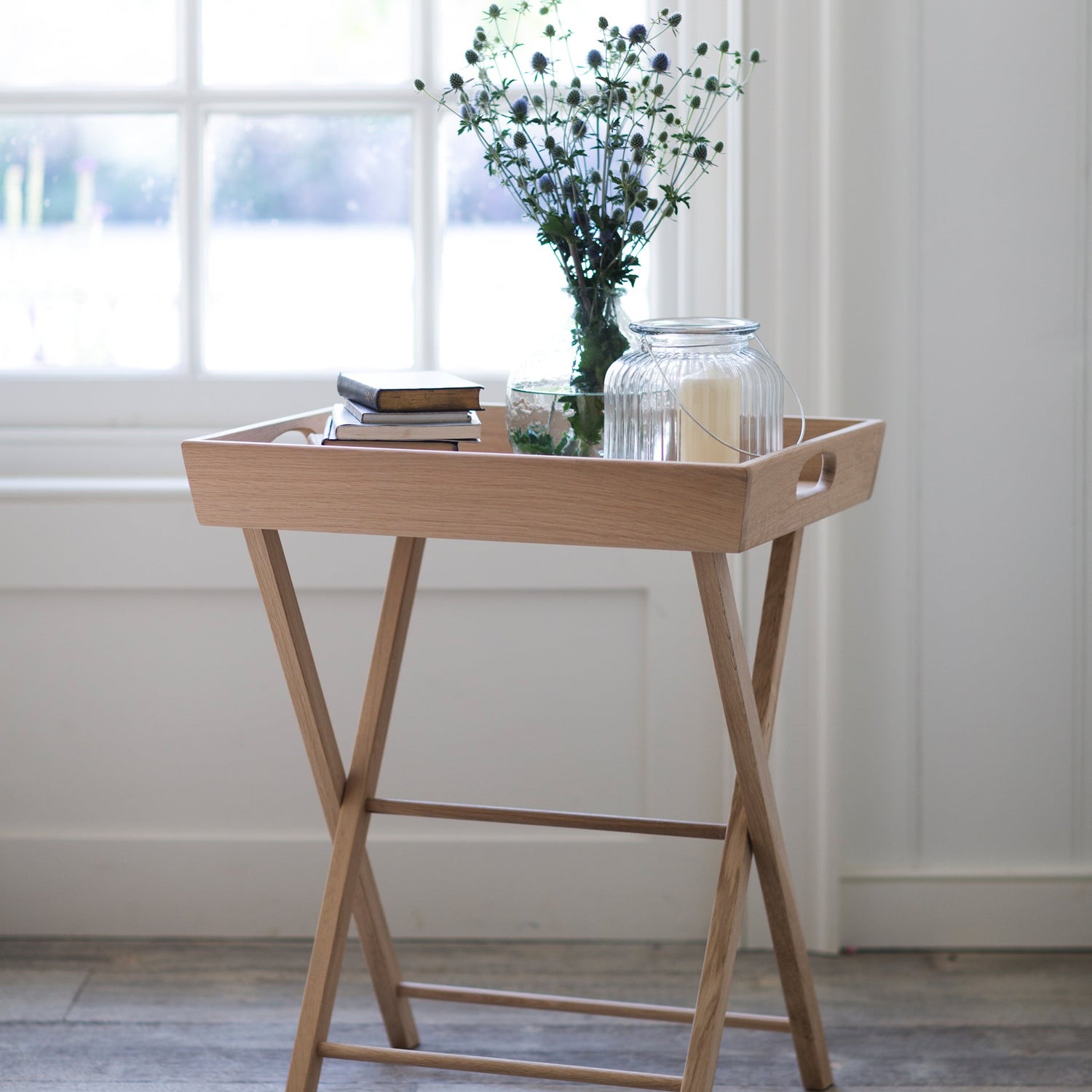 Wooden tray table with a vase of flowers and books in a bright room.