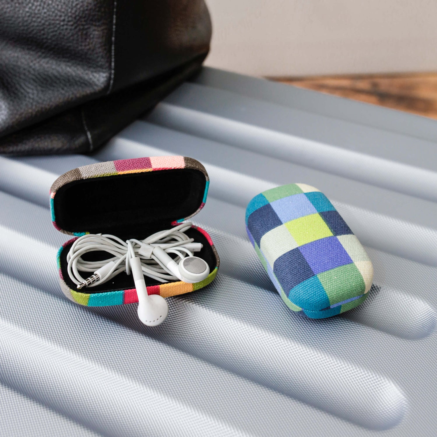 Colorful checkered earbud case with earphones on a textured surface