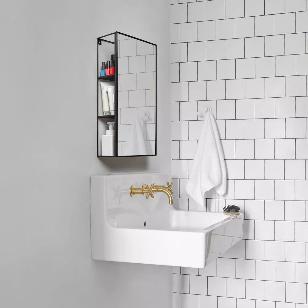 Bathroom with white tiled walls, a white sink with gold faucet, and a black shelf with toiletries.