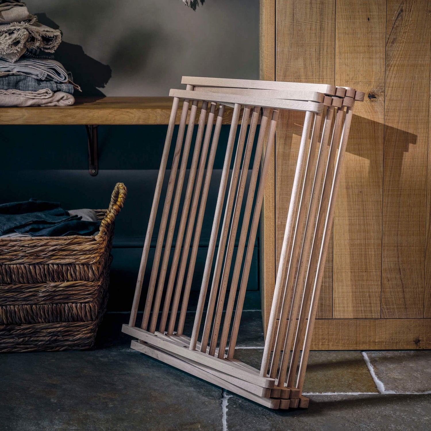 Wooden clothing rack against a wooden wall with shelves and a basket in the background.