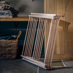 Wooden clothing rack against a wooden wall with shelves and a basket in the background.