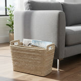 Rattan basket with magazines on a wooden floor next to a gray sofa.