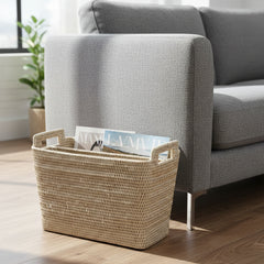 Rattan basket with magazines on a wooden floor next to a gray sofa.