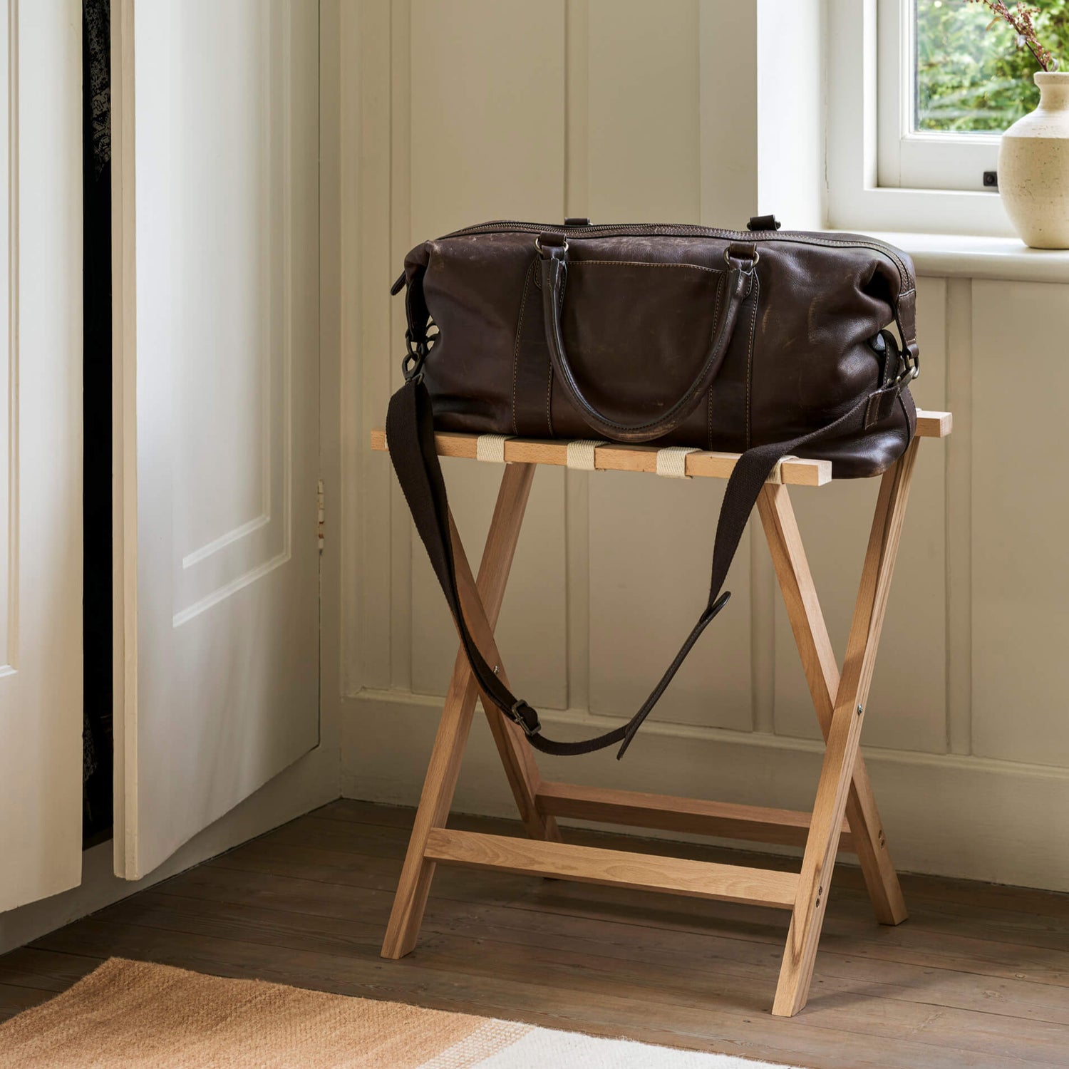 Brown leather bag on a wooden stand in a room with a window and plant.