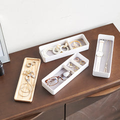 Jewelry and accessories organized in white and wooden trays on a wooden surface.